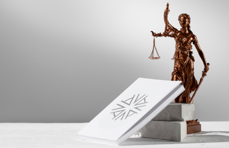 gold statue of Justice, statue of lady justice representing due diligence and law and order on a white marble table with a white book leaning against the base of the statue bearing the Astons brand