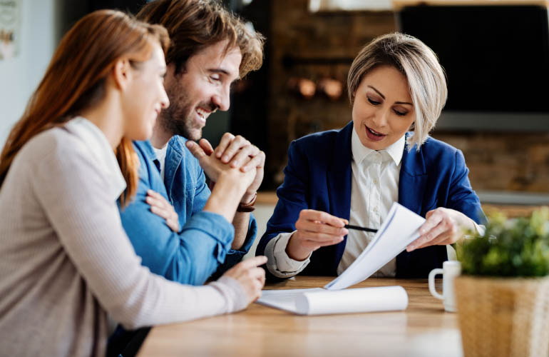 A man and a women which appear to be a couple sitting at a table discussing a contract with a female banking or finance expert. The process is demonstrating a step in the due diligence process that is typical in citizenship by investment and residency by investment programs offered by Astons